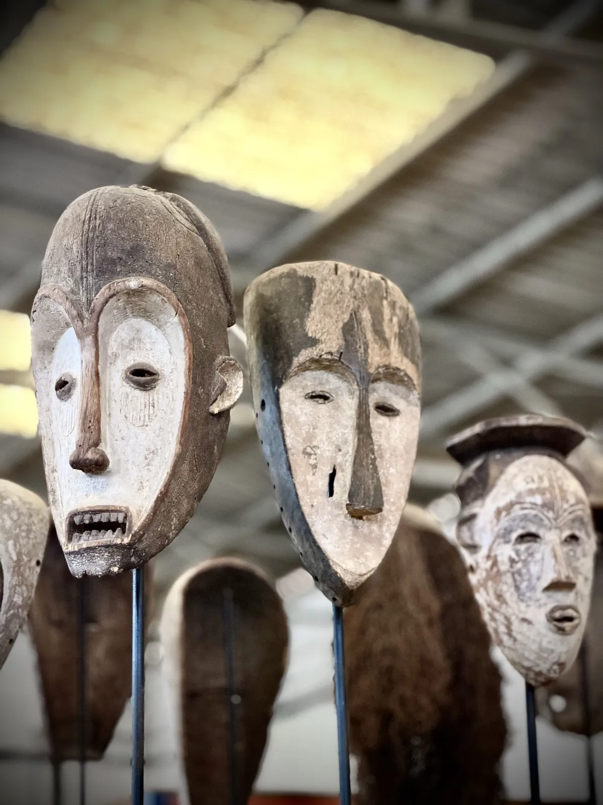Tall carved masks seen against warehouse light